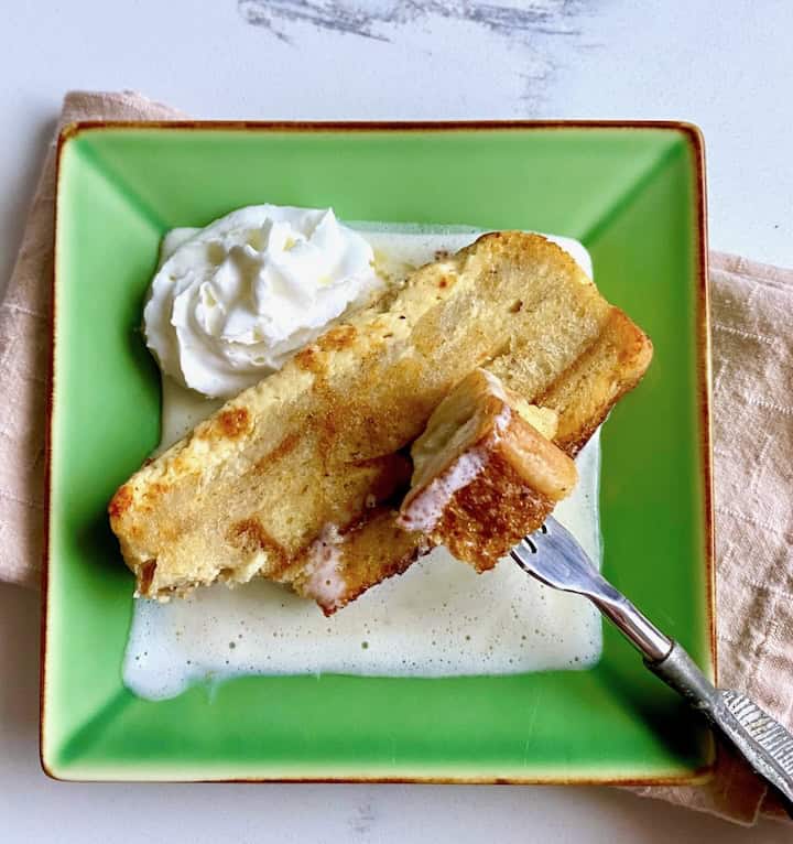 Slice of white chocolate bread pudding on melted ice cream.