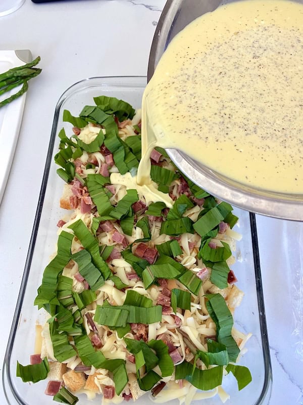 Pouring egg mixture on casserole layers.