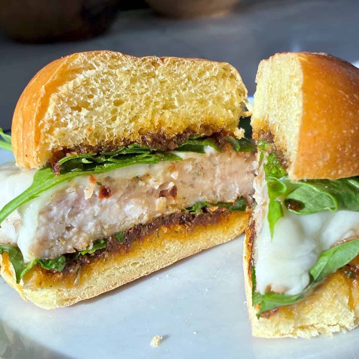 A chicken burger with arugula and cheese on a white plate.