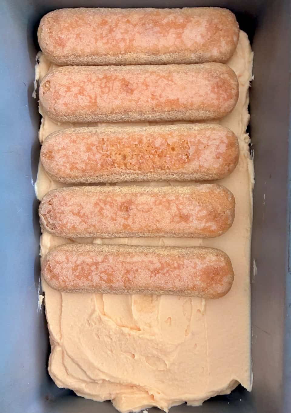 Layering lady fingers and filling in a loaf pan.