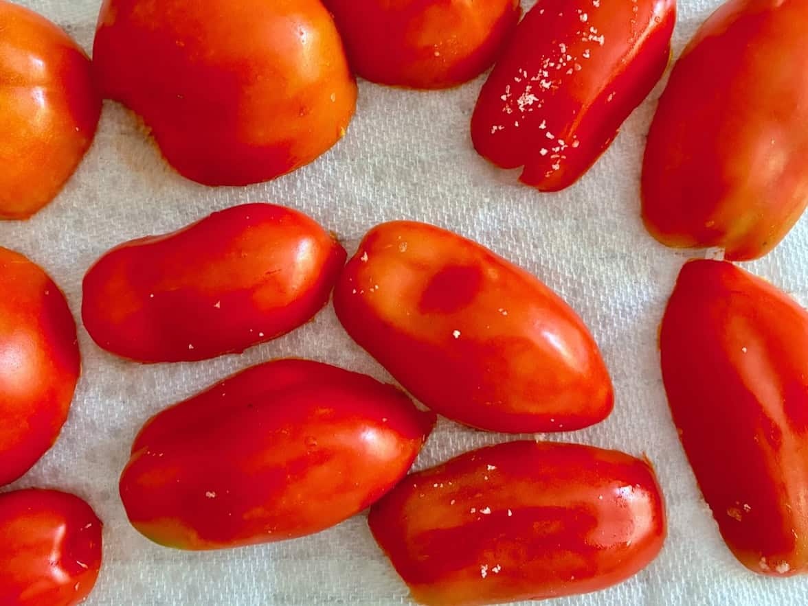 Sliced and salted tomatoes draining on paper towels.