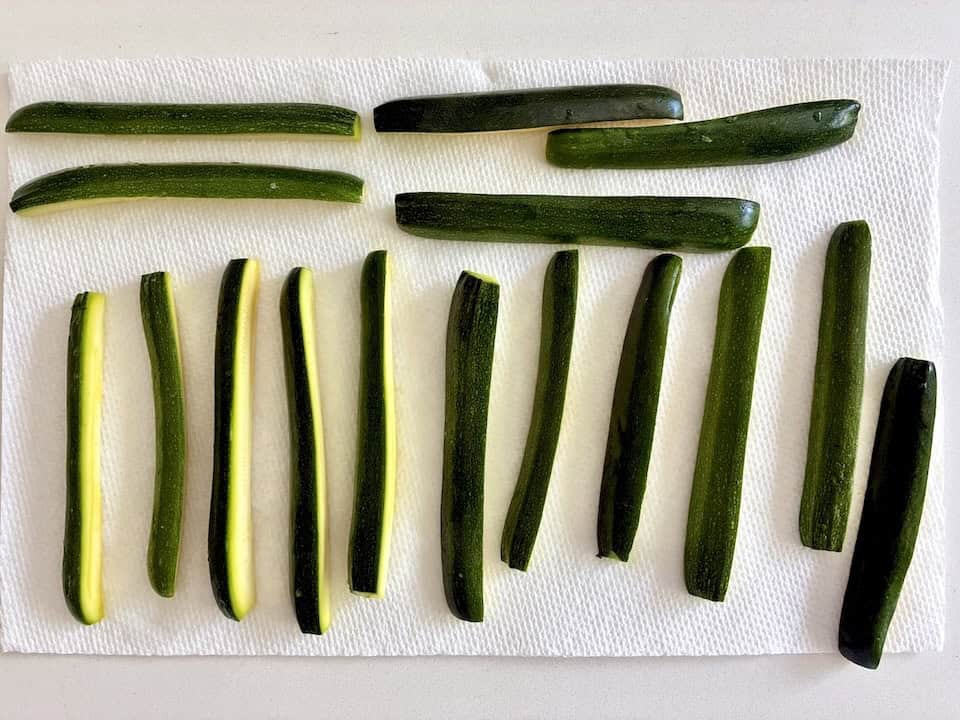 Several zucchini cut into strips on a paper towel.
