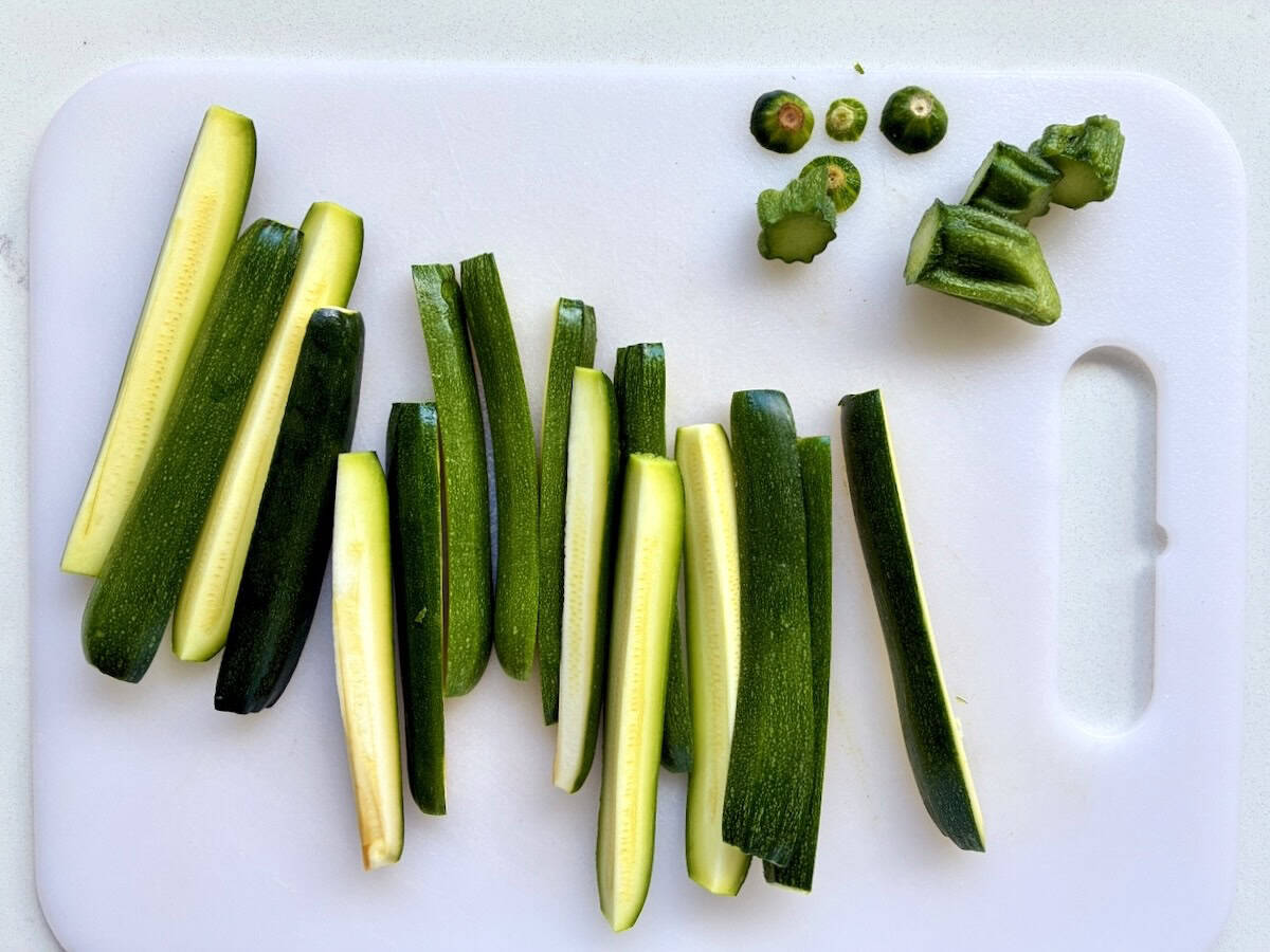 Zucchini cut into spears on a cutting board.