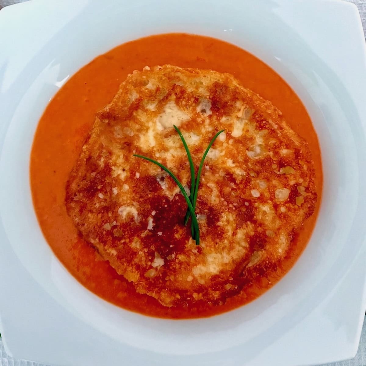 Tomato and grilled cheese soup garnished with chives.