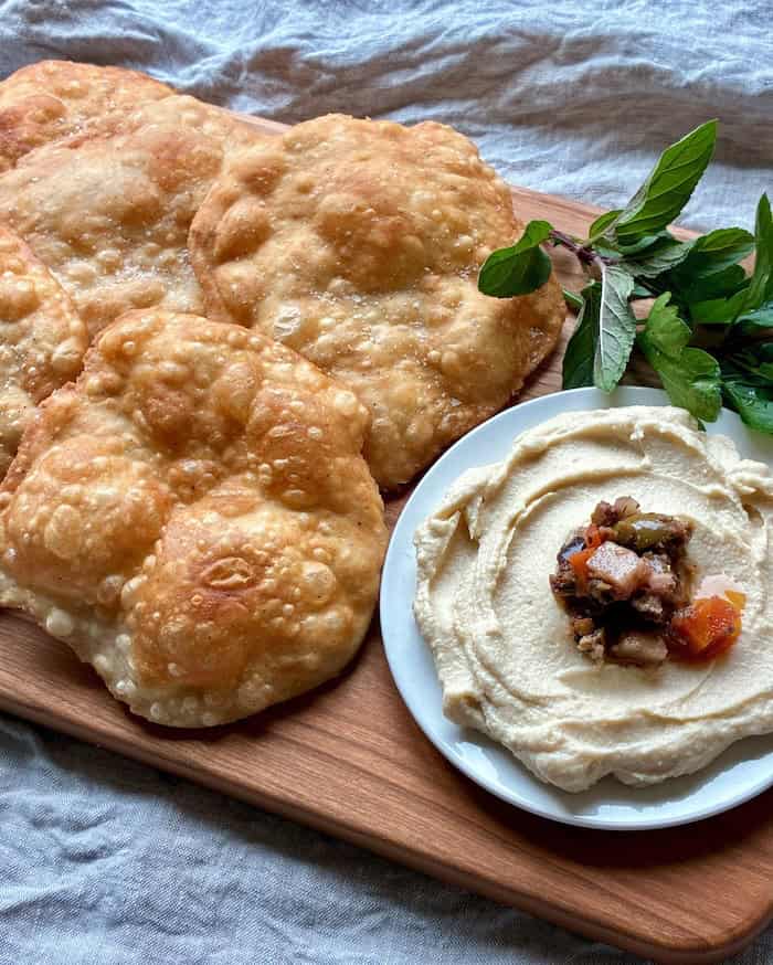 Freshly fried Indian flatbreads with a side of creamy hummus and fresh herbs.