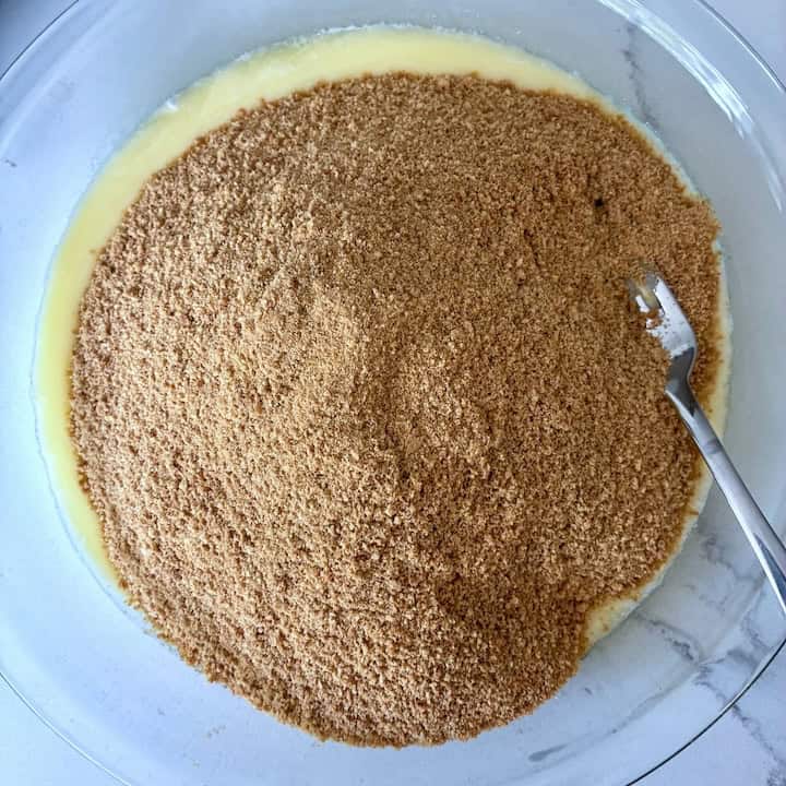 Mixing cookie crumbs and butter in a pie plate.