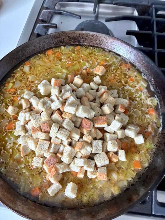 Adding croutons to the vegetable and broth mixture.